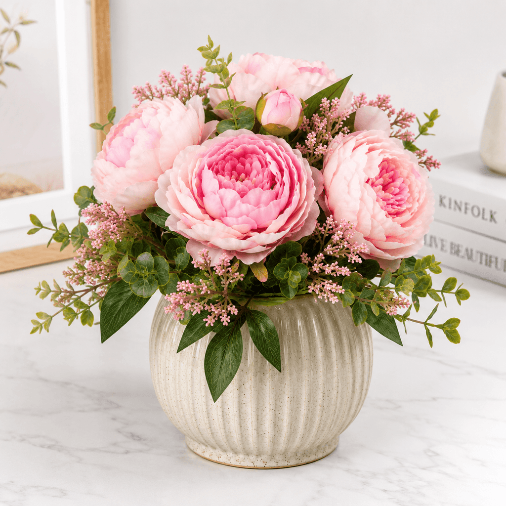 Pink peony flower arrangement in a textured vase on a light surface.