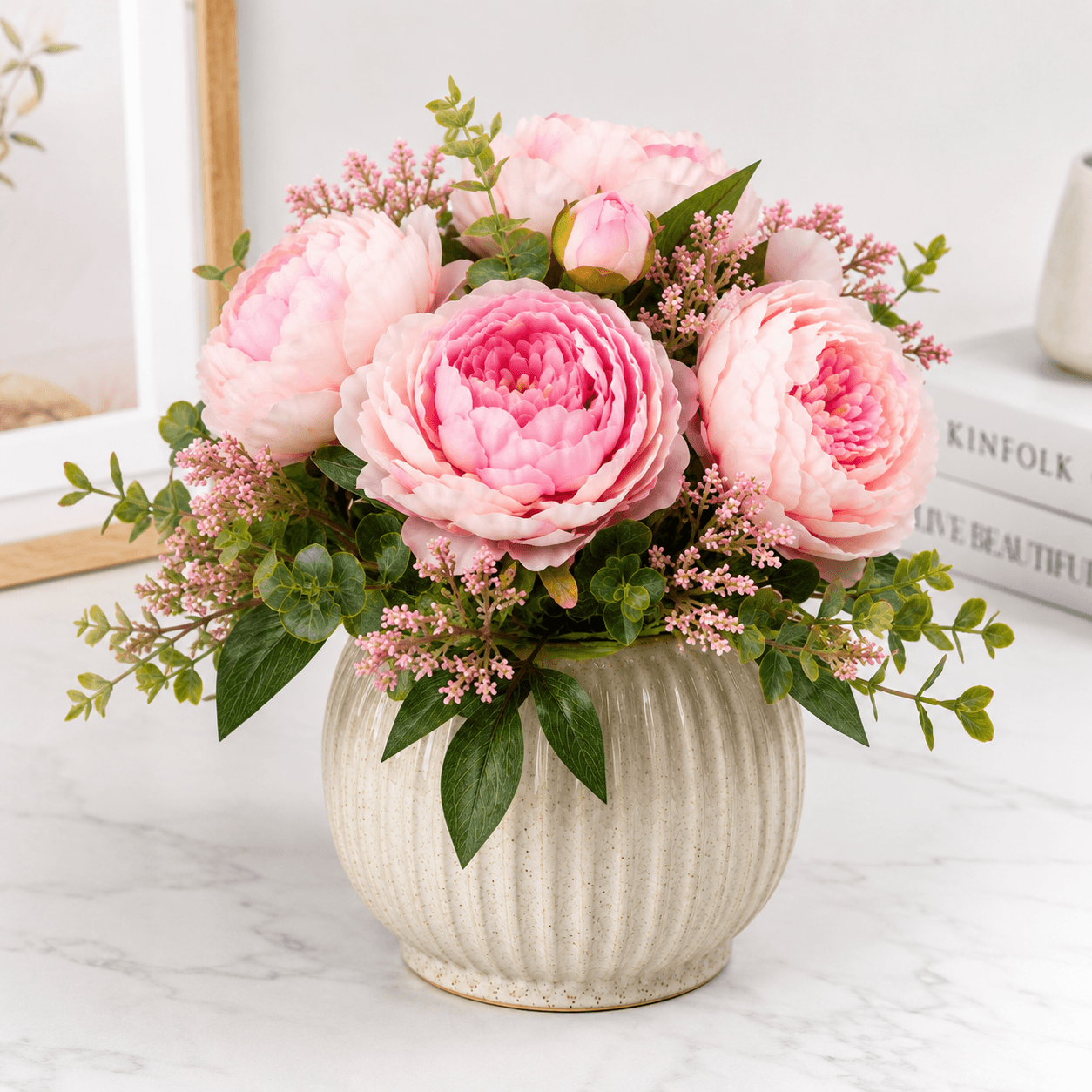 Pink peony flower arrangement in a textured vase on a light surface.